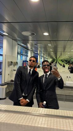 two men in suits are taking a selfie with their cell phones at an airport