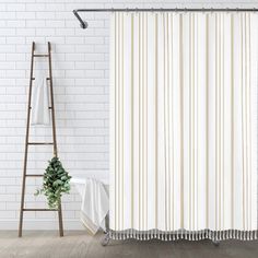 a white shower curtain hanging on a brick wall next to a ladder and potted plant