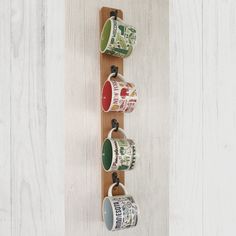 three coffee mugs are hanging on a wooden shelf with hooks and clips to hold them