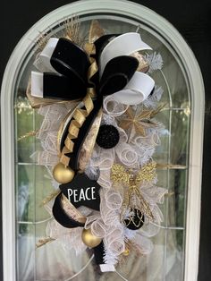 a wreath with black, white and gold decorations hanging on the front door for peace