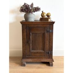 a wooden cabinet sitting on top of a hard wood floor next to a vase filled with flowers