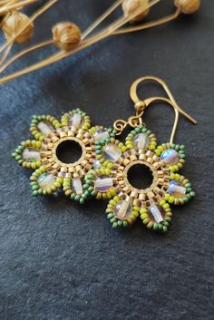 two pairs of earrings sitting on top of a black surface next to dried flowers and leaves