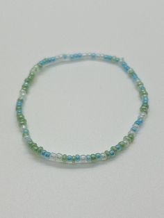 a beaded bracelet with blue and green beads on a white surface, in the shape of a circle