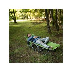 a man laying on top of a green lawn chair in the middle of a forest