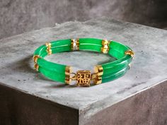 Our 'Double Fu Fuku Fortune Jade Bracelet' embodies radiance and stature, with hand carved jade lengths intertwined with 14K Gold; a unisex statement. The two layers of cylindrical Jade tubes stands for courage and strength.   Our top craftsman signs off the piece with a crafted symbol of fortune at the clasp. The Han symbol for fortune and luck evokes an unrivaled sense of positivity and happiness.  Materials: 3.00g 14K Gold and 16.40g Jadeite (Approximately) Dimensions: 185 x 10 x 8 mm Gross W Luxury Jade Bracelets For Formal Occasions, Luxury Formal Jade Bracelets, Luxury Jade Jewelry, Luxury Gold Jade Bracelets, Chinese Bracelet, Purple Vase, Jade Dragon, Purple Jade, Carved Jade