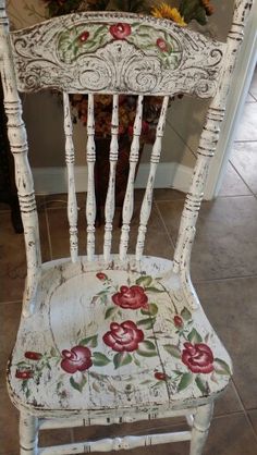 an old white chair with flowers painted on the seat and back side, sitting in front of a door