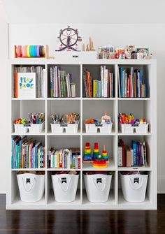 a white bookcase filled with lots of books and plastic containers on top of it