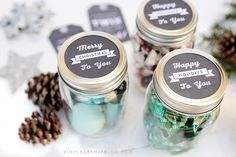 three mason jars filled with candy sitting next to pine cones and christmas tree ornaments on a white surface