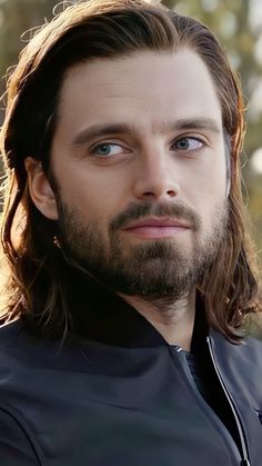 a man with long hair and blue eyes looks at the camera while wearing a leather jacket