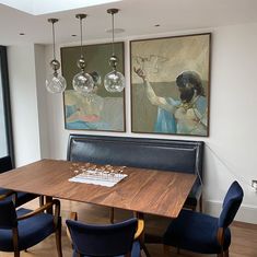 a dining room table with blue chairs and artwork hanging on the wall above it, along with two chandeliers