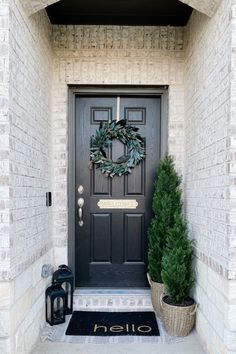 a black door with a wreath on it and two potted plants in front of it