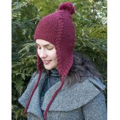 a woman wearing a red knitted hat next to a tree with leaves on it