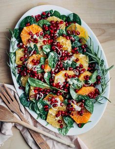 a white plate topped with oranges and spinach salad next to two wooden utensils