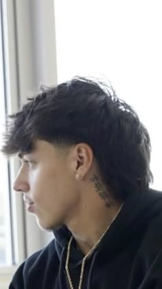 a man with black hair and tattoos sitting in front of a window looking out the window