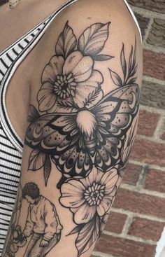 a woman's arm with flowers and a butterfly tattoo on her left arm, next to a brick wall