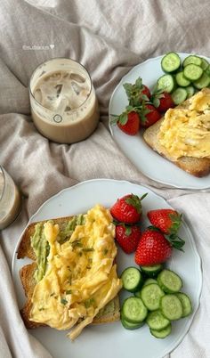 two white plates topped with sandwiches and fruit next to a cup of coffee on a bed