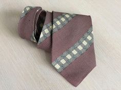 Stylish vintage tie from Gordon Crane, crafted from 100% silk. This tie features a classic reddish brown background with beige and green checkered stripes, giving it a timeless appeal with a touch of retro sophistication. Perfect for both formal occasions and adding a vintage edge to casual outfits, the fine craftsmanship and all-silk fabric make it a luxurious addition to any collection. This unique piece is an ideal choice for anyone looking to add a statement accessory to their attire. Length Luxury Striped Suit And Tie Accessories, Luxury Classic Green Suit And Tie Accessories, Luxury Brown Classic Suit And Tie Accessories, Luxury Classic Brown Suit And Tie Accessories, Beige And Green, Green Checkered, Vintage Tie, Brown Background, Retro Stripes