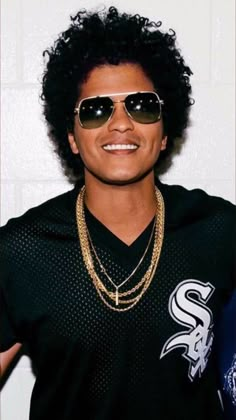 a man wearing sunglasses and a black shirt with gold chains on his neck is smiling at the camera