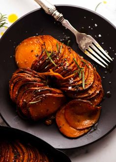 a black plate topped with sliced up sweet potatoes next to a fork and knife on top of a table