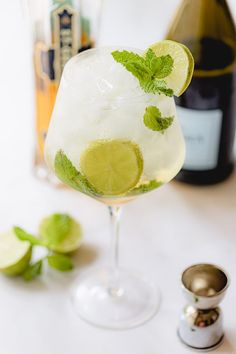 a drink with lime and mint garnish in a glass next to a bottle