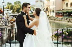 a bride and groom standing next to each other in front of a bridge with flowers