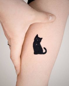 a black cat tattoo on the left side of the arm, with its tail curled up