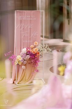 a welcome sign with flowers on it sitting in front of a pink curtained entrance