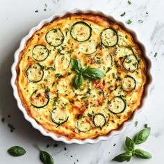 a quiche with zucchini and cheese in a white dish on a marble surface