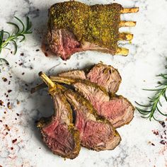 two pieces of meat on a table with herbs and seasoning next to the steak