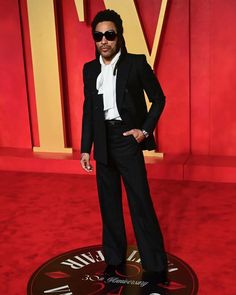 a man in a suit and sunglasses standing on a red carpet with his hands in his pockets