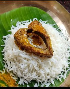 a plate with rice, meat and sauces on it in a metal bowl next to a green leaf