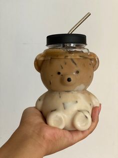 a hand holding a small teddy bear in a jar with a straw sticking out of it