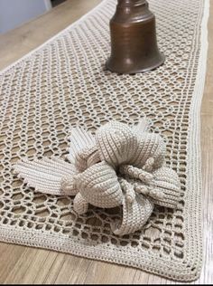 a crocheted table runner with a flower on it and a bell in the background