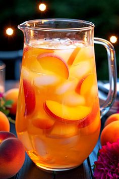 a pitcher filled with liquid sitting on top of a table next to peaches and flowers