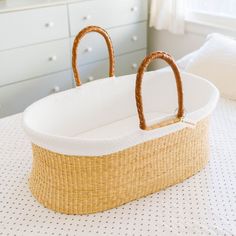 a baby's bassinet with two handles sitting on top of a bed