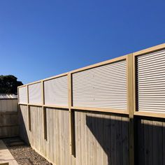 a wooden fence with slatted panels on the top and bottom part, along side a gravel path