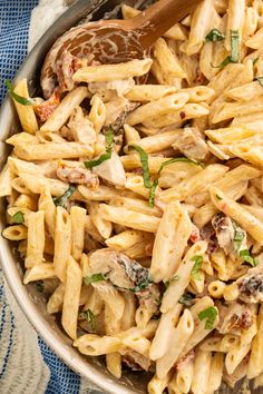 a pan filled with pasta and chicken on top of a blue towel next to a wooden spoon