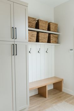 a room with white cabinets and baskets on the wall, along with a wooden bench