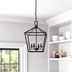 a chandelier hanging from the ceiling in a kitchen with white walls and open shelves