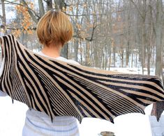 a woman holding up a black and white striped shawl over her shoulders in the snow