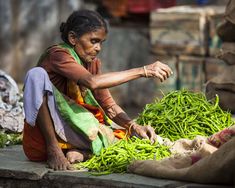 an old woman sitting on the ground with some green beans in front of her,