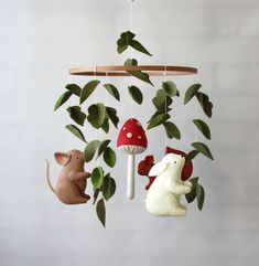 three stuffed animals hanging from a tree branch with leaves and mushrooms in the air above them