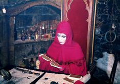 a woman dressed in red is sitting at a table with bottles and papers on it