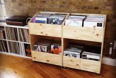 two wooden shelves holding records and cds in front of a brick wall with wood flooring