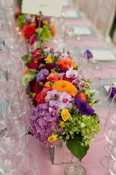 the table is set with many different colored flowers and wine glasses on top of it