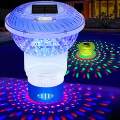 a solar powered light up projector with colorful lights on it's sides and in the background is a swimming pool