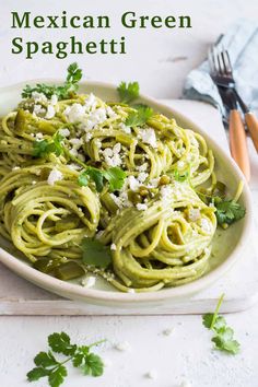 a white plate topped with green pasta covered in fettuccine and parsley