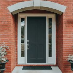 a black door and two planters on the side of a brick building with white trim