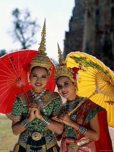 two women dressed in traditional thai garb holding umbrellas and posing for the camera