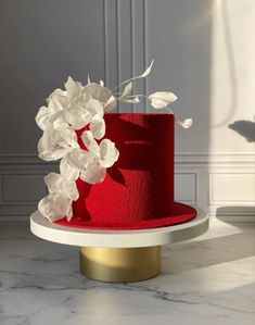 a red cake with white flowers on top sitting on a table next to a wall